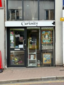 picture of shopfront with white banner above glass doorway, black text saying Curiosity