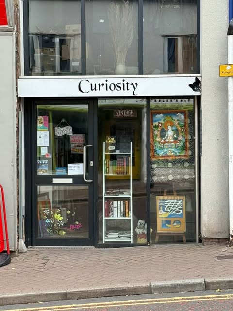 picture of shopfront with white banner above glass doorway, black text saying Curiosity