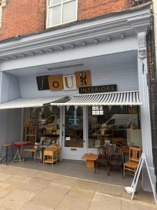 Picture of shopfront with striped blue and white awning, wooden furnitaure either side of doorway and building painted light blue