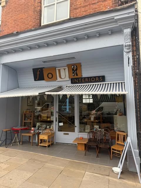 Picture of shopfront with striped blue and white awning, wooden furnitaure either side of doorway and building painted light blue