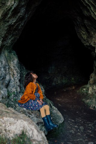 little girl sitting on a rock in a cave enterance, looking up